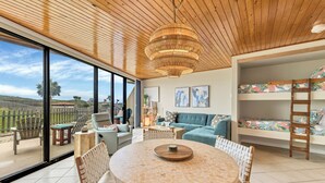 Un vaste espace de vie comprenant une table ronde, des sièges confortables, un canapé et un lit superposé avec une literie aux couleurs vives.