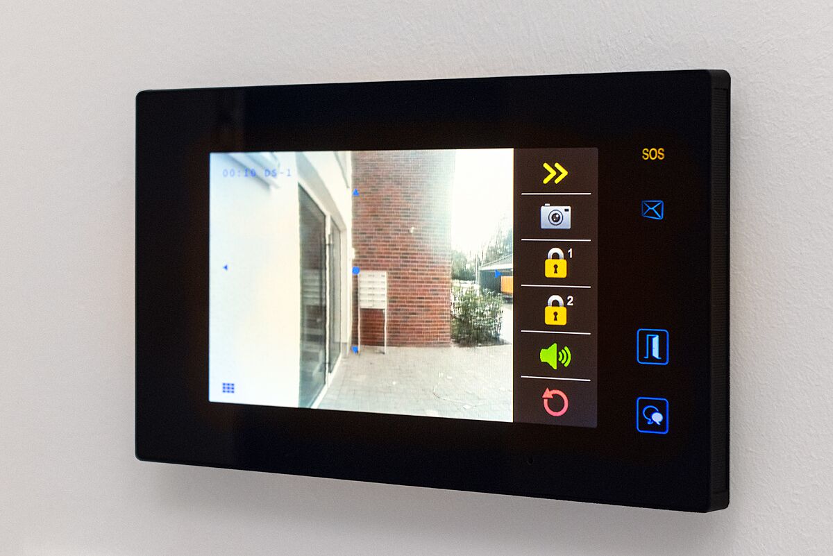Une caméra de surveillance filmant l’entrée d’un bâtiment, dotée d’un bouton d’appel d’urgence et de divers icônes de contrôle.