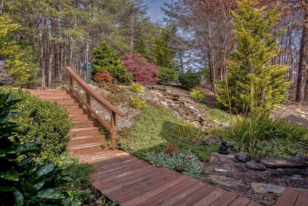 A wooden staircase leading up a rocky hill, surrounded by various types of trees and shrubs.