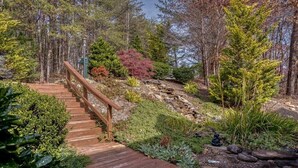 A wooden staircase leading up a rocky hill, surrounded by various types of trees and shrubs.