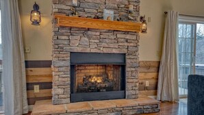 A stone fireplace with a wooden mantel shelf, a fire burning inside, and a stone wall with a wooden panel design.