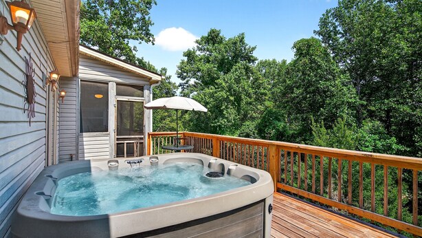 A hot tub on a wooden deck with a glass door leading to an outdoor seating area.