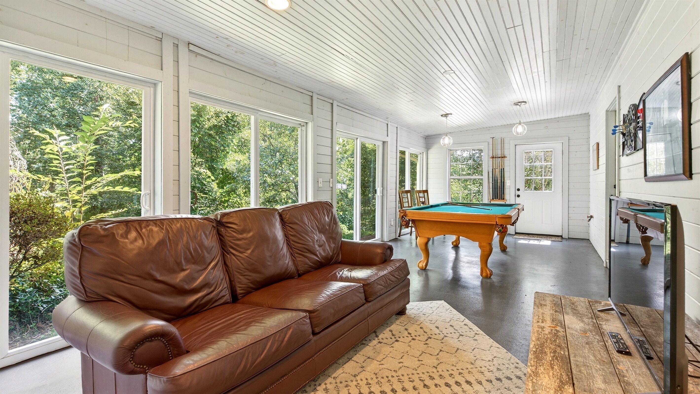 A spacious room with a brown leather sofa, a pool table, and a billiards rack.