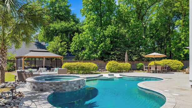 A backyard with a swimming pool, a covered seating area, and a patio with outdoor furniture. - Pleasant Place New Build + Pool Great for Families (Mount Pleasant)
