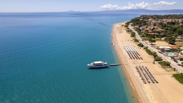 A coastal area with a beach, a boat docked near the shore, and a row of beachside buildings. - Beachfront Villa Alexandra (Σκάλα)
