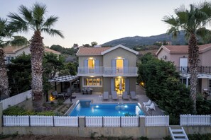 Una casa de dos pisos con piscina, mobiliario exterior y cerca de piquetes blancos.