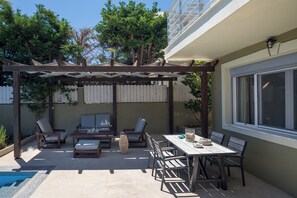 Un patio con pérgola, mobiliario exterior, piscina y zona de comedor.