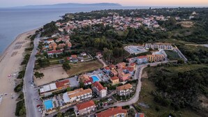 An aerial view of a coastal town with a beach, residential buildings, and a swimming pool complex. - Beachfront Villa Alexandra (Σκάλα)