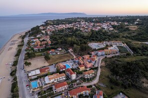 An aerial view of a coastal town with a beach, residential buildings, and a swimming pool complex.