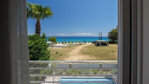 A view from a balcony overlooking a beach with a clear sky, a palm tree, and a swimming pool. - Beachfront Villa Alexandra (Σκάλα)