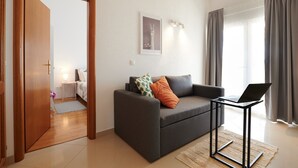 Ein modernes Wohnzimmer mit einem grauen Sofa, einem Laptop auf einem Beistelltisch und einem Spiegel, der den Raum reflektiert.