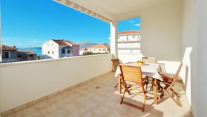 Ein Balkon mit Tisch und Stühlen, Blick auf das Meer und Gebäude, und ein gefliester Boden.