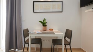 Ein Essbereich mit einem weißen Tisch, zwei schwarzen Stühlen, einer Topfpflanze und einem gerahmten Bild von Tieren an der Wand.