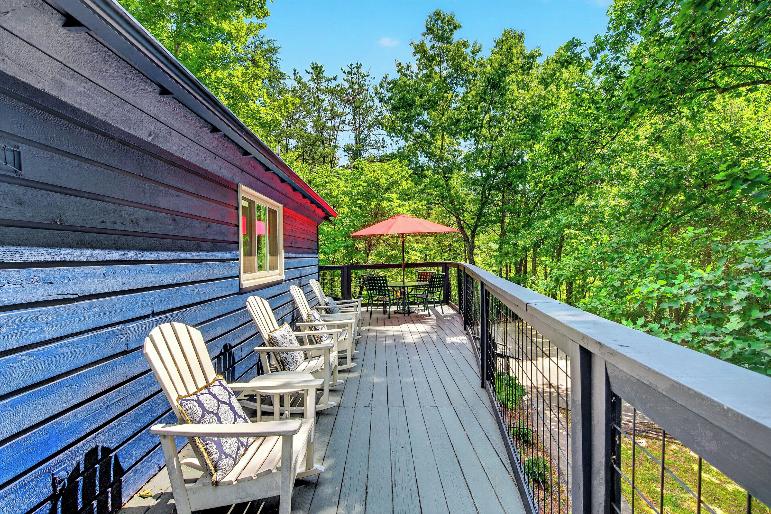 A wooden deck with Adirondack chairs and a red umbrella.