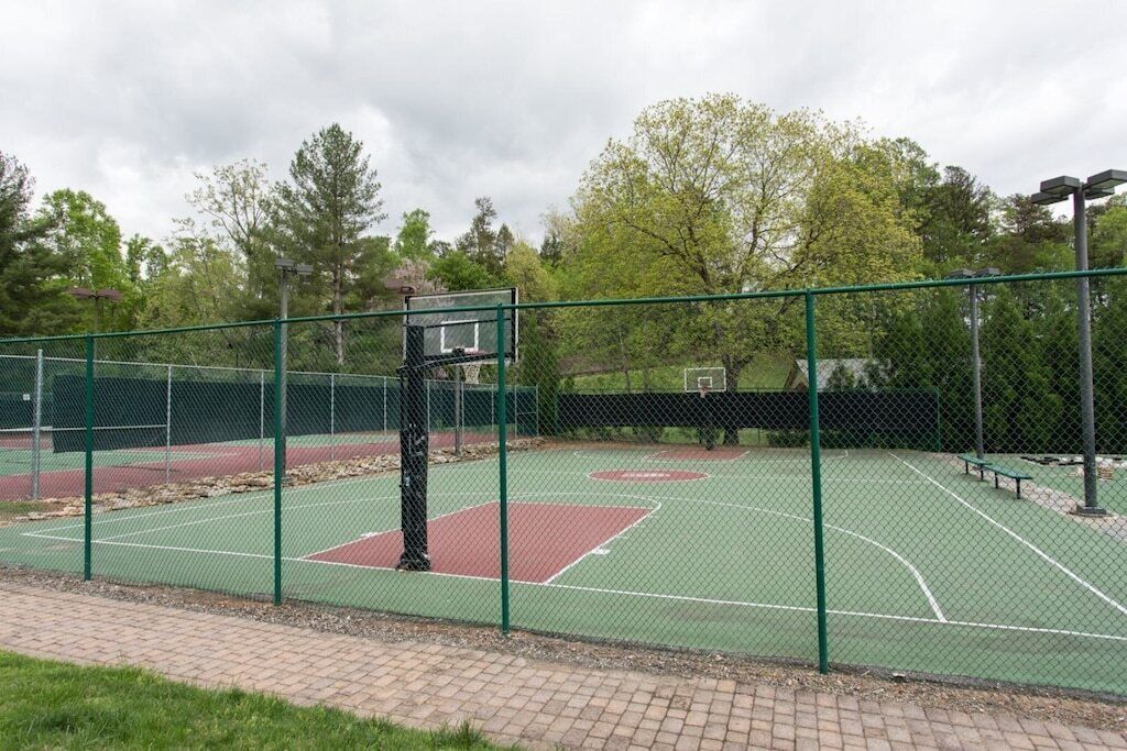 Een basketbalveld buiten met een groene omheining, een basketbalring en een bankje.