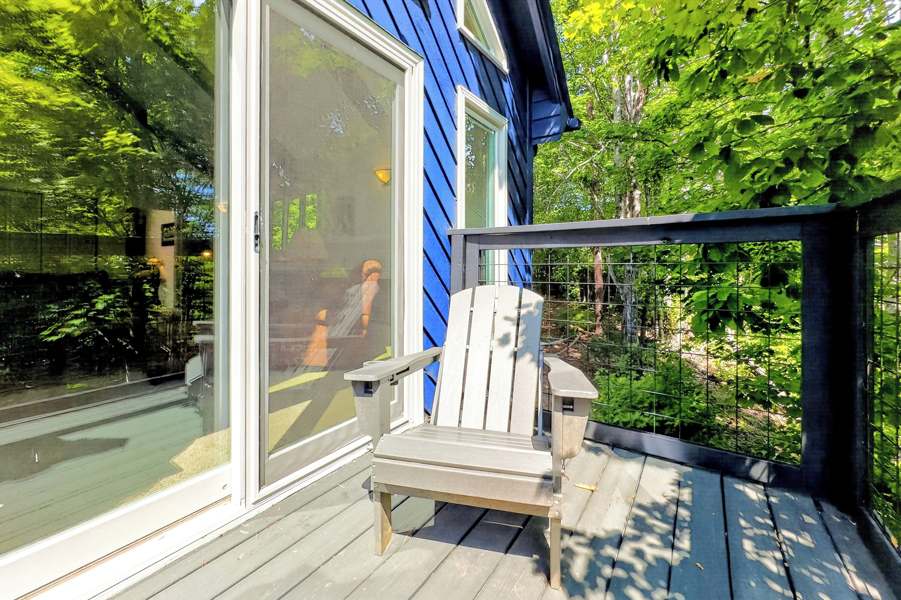 A wooden deck with a single Adirondack chair, a glass door, and a blue building in the background.