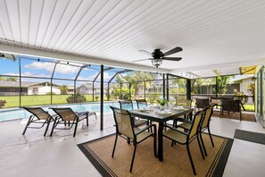 An indoor patio area with a pool view, a ceiling fan, and a dining table with chairs. - Seaside Villa Cape Landing 3 Bedroom, 2 with Smart TV and King Size Bed (Cape Coral)