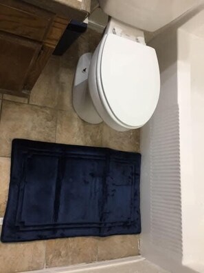 A bathroom with a toilet, a blue bath mat, and a tiled wall.