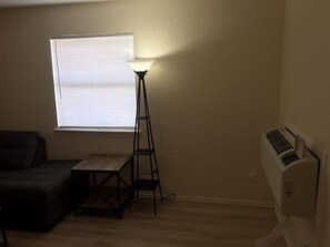 Une petite pièce avec une fenêtre, un lampadaire, un radiateur et un canapé.