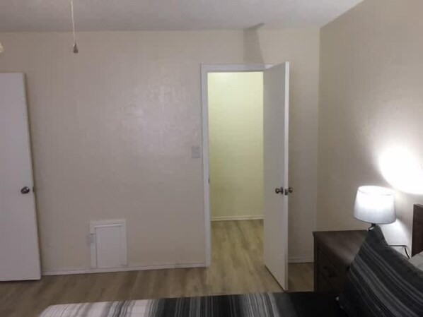 A room with a bed, a bedside table, a lamp, a door, and a hallway leading to another room. - Cozy 1-BR upstairs apartment, near Fort Sill! (Lawton)