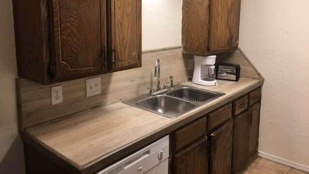 Una cocina con armarios de madera, un lavamanos de acero inoxidable y un lavavajillas integrado.