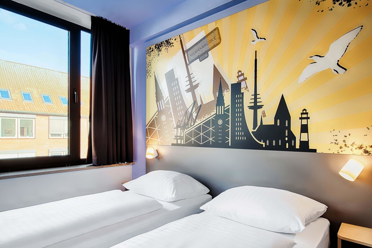Ein Hotelzimmer mit zwei Betten, einem großen Fenster und einem Stadtbild-Wandgemälde.