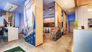 A modern hotel lobby with a reception desk, seating area, and a large wall mural.