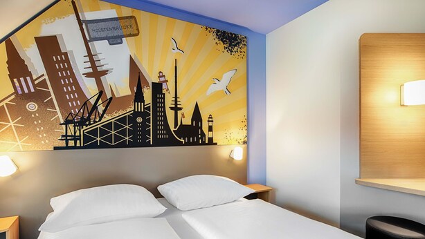 Une chambre d’hôtel comprenant un lit, deux tables de chevet, une fresque murale et une petite table d’appoint.