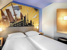 Una habitación de hotel con una cama, dos mesitas de noche, un mural en la pared y una mesita auxiliar.