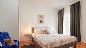 A bedroom with a bed, two bedside tables, a lamp, a hat on a chair, and a window with curtains. - PRGA 3, sea view apartment, 60m from pebble beach Copacaba (Okrug Gornji)