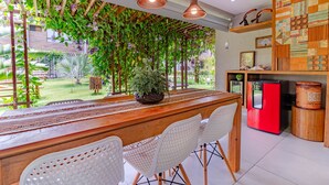 A kitchen with a wooden table, white chairs, hanging plants, and a red refrigerator. - IT11 Ap 3 Quartos a 50m da Praia (Camaçari)
