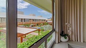 A balcony with a view of a courtyard, a wooden table, and a potted orchid. - IT11 Ap 3 Quartos a 50m da Praia (Camaçari)