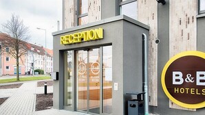 Aula, jossa on lasiovi, B&B Hotels -kyltti ja moderni rakennuksen julkisivu.