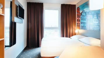 Una habitación de hotel con una cama, un televisor montado en la pared, una ventana con cortinas y un cuadro en la pared.