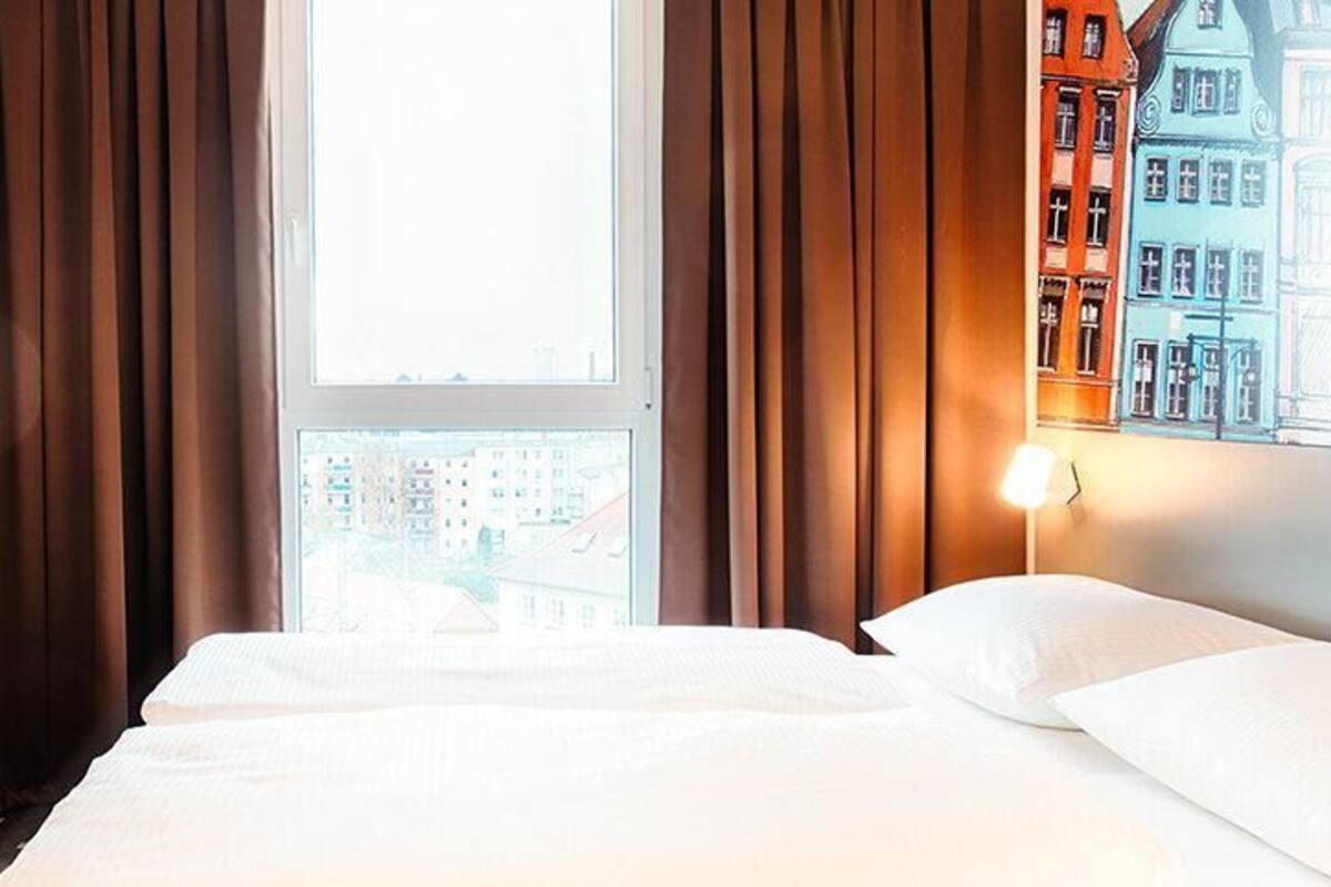 Habitación de hotel con cama, cortinas, televisor y ventana con vista a la ciudad.