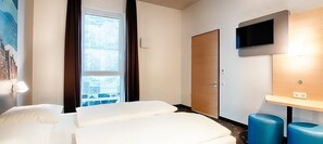 A hotel room with a bed, a TV mounted on the wall, a window with curtains, and a door. - B&B Hotel Rostock City-West (Rostock)