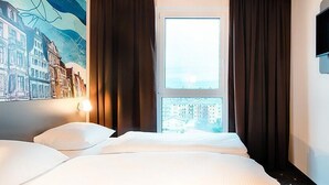 Hotellihuone, jossa on suuri sänky, seinälle asennettu televisio ja ikkuna, jossa on verhot.