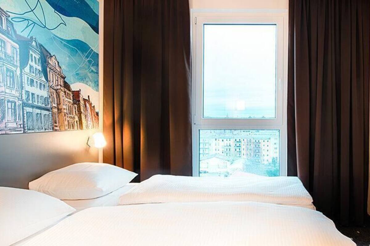 Una habitación de hotel con una cama grande, un televisor montado en la pared y una ventana con cortinas.