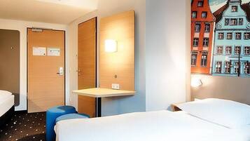 A hotel room with two beds, a small table, and a wall-mounted light.