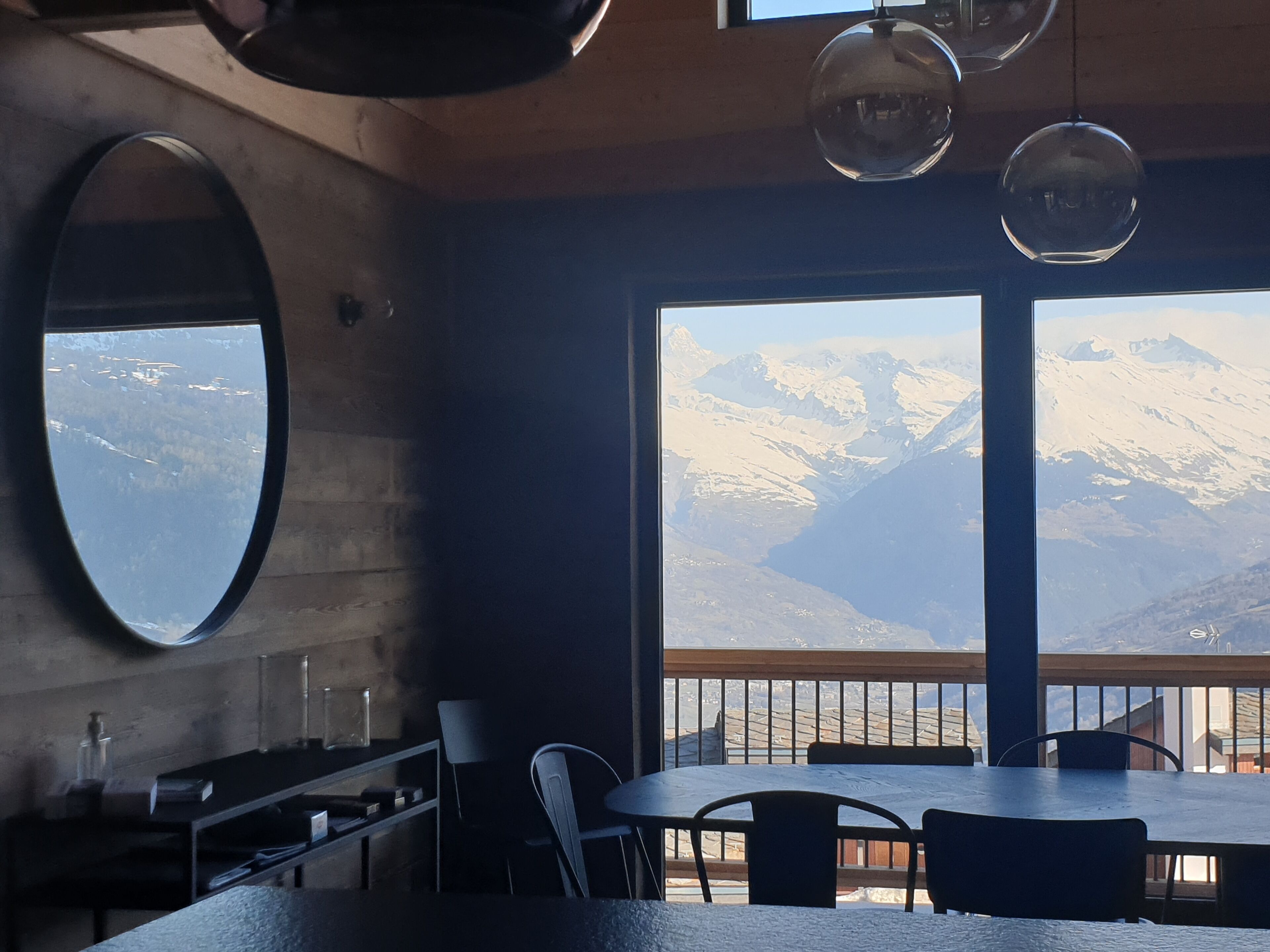 Un restaurant offrant une vue sur les montagnes enneigées grâce à de grandes fenêtres.