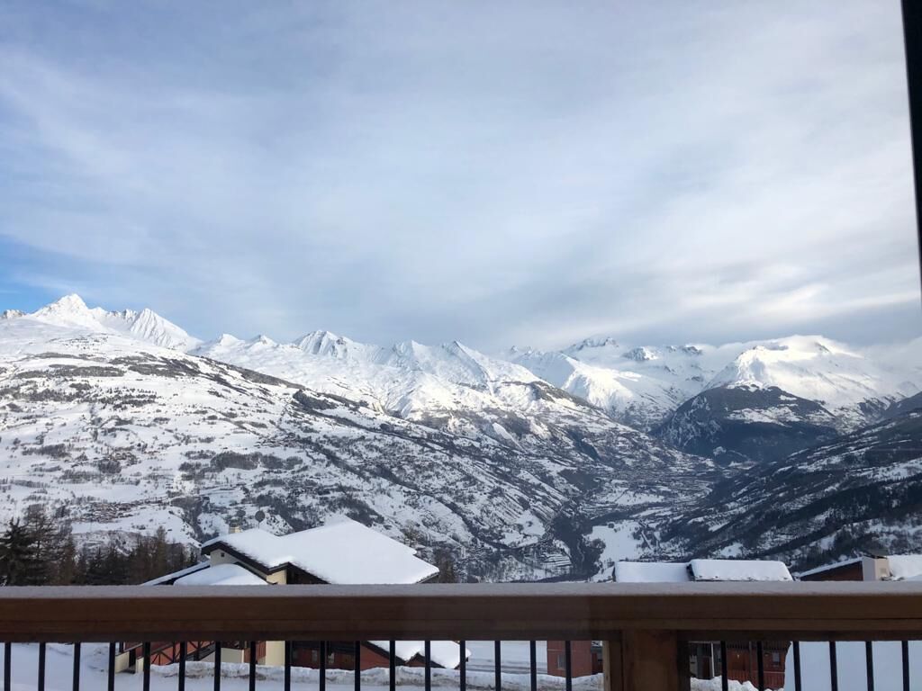 A mountain landscape with snow-covered peaks and a wooden balcony railing.