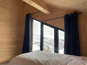 A wooden cabin room with a bed, large windows, and curtains. - SKI IN SKI OUT PARADISKI LA PLAGNE LES COCHES TOP OF THE RANGE CHALET (Bellentre)