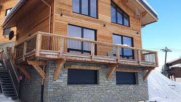 Un chalet en bois doté d’un balcon, avec des fondations en pierre et un ciel d’un bleu éclatant.