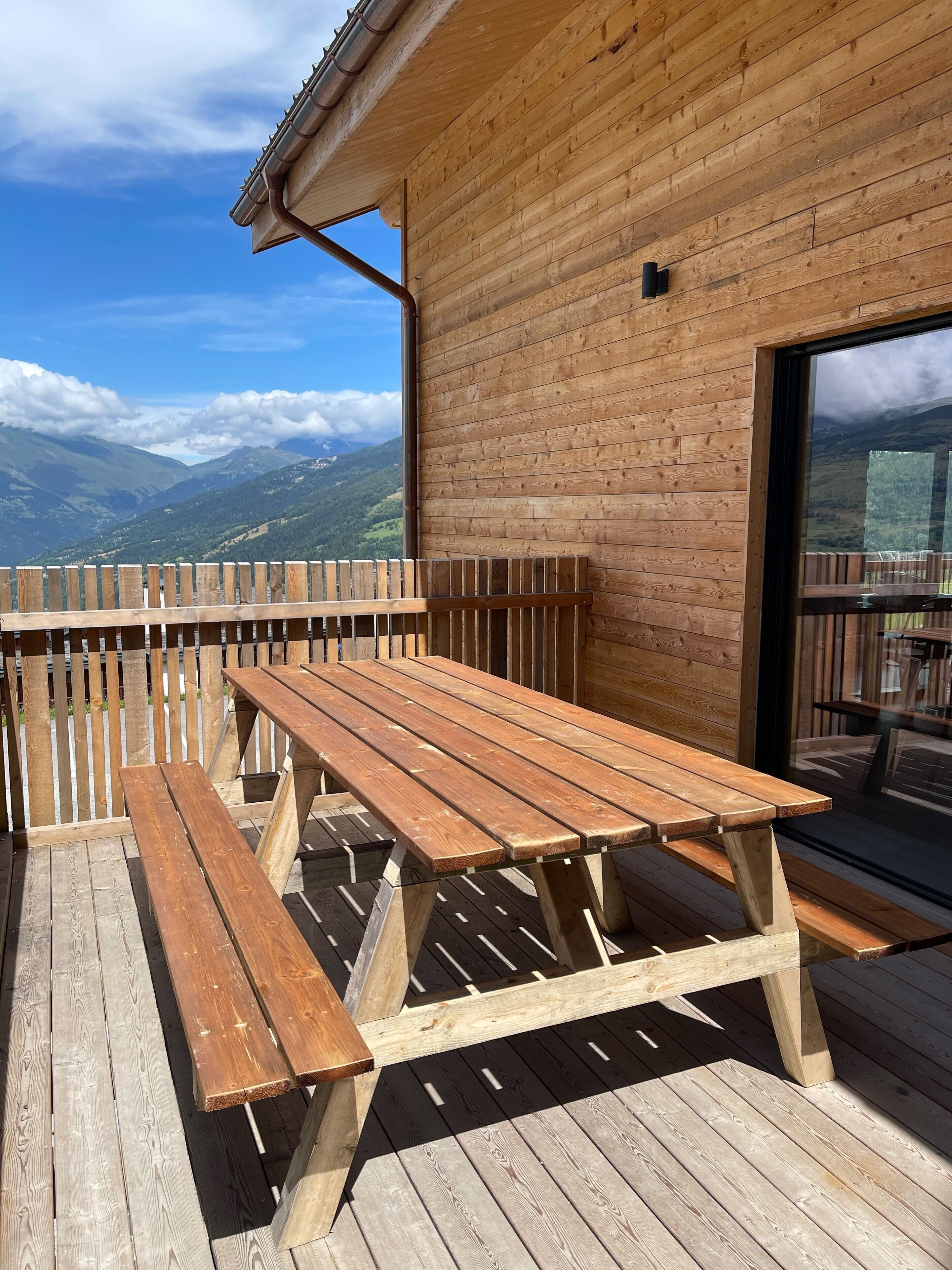 Une terrasse en bois avec des tables de pique-nique et une vue sur les montagnes.