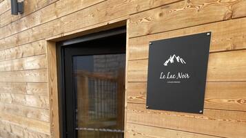 Un mur extérieur en bois, avec une porte noire et une enseigne sur laquelle on peut lire « Le Lac Noir ».