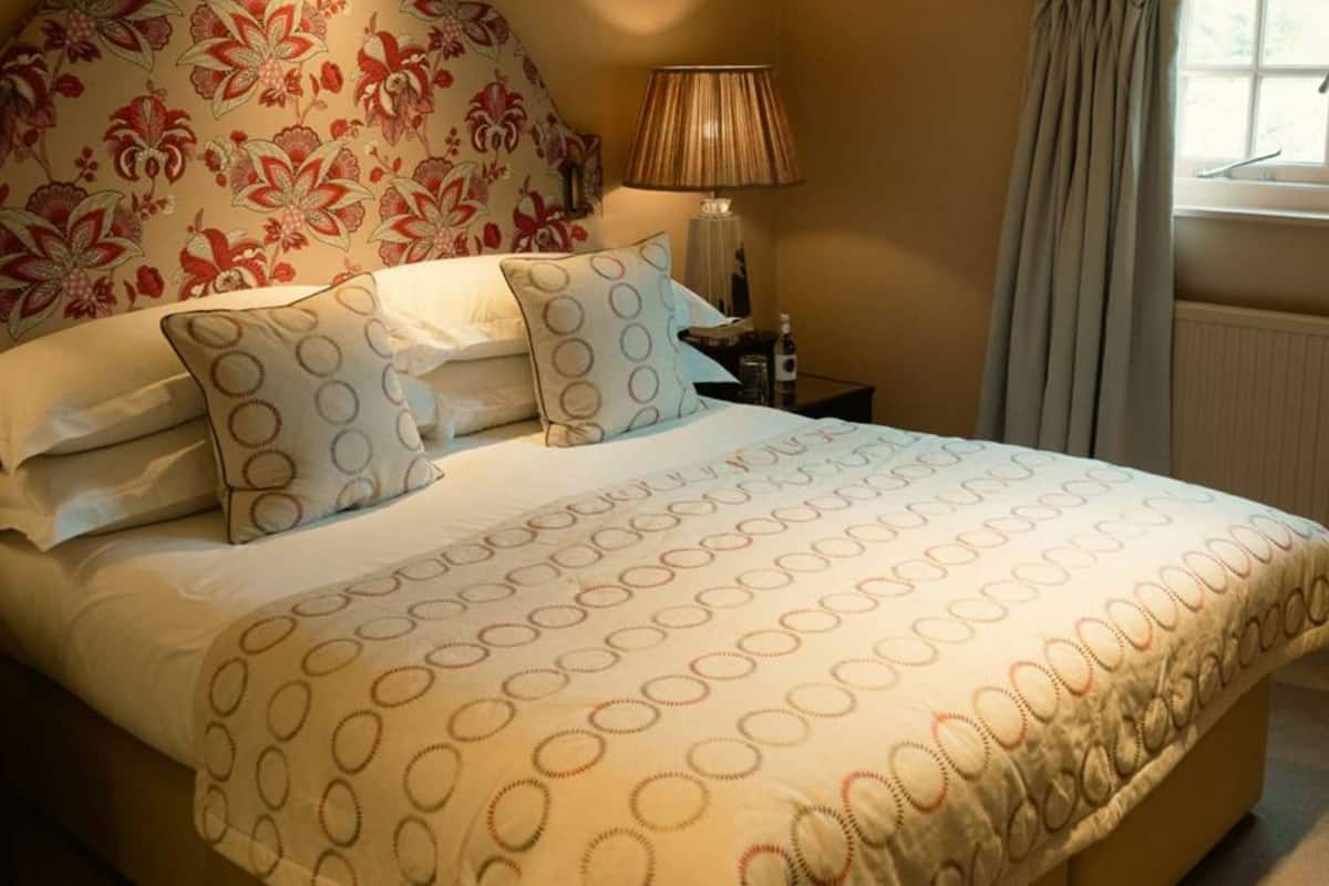 Una cama bien hecha con una colcha estampada, un cabecero floral y una lámpara de noche.