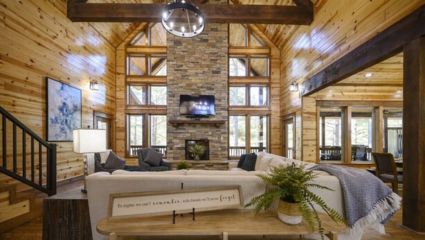 L’intérieur chaleureux d’un chalet avec une cheminée en pierre, des murs en bois et une grande fenêtre donnant sur une forêt.