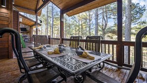 Un espace extérieur abrité, aménagé pour les repas, avec une terrasse en bois, des chaises en métal et une table dressée pour deux personnes.