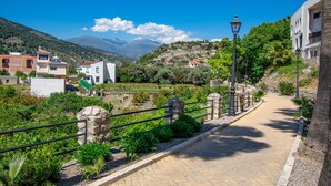 Un camino pavimentado con barandillas de piedra, rodeado de vegetación y edificios.