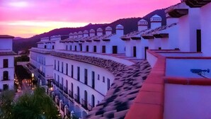 Una hilera de edificios blancos de arquitectura uniforme, cielo despejado y una cadena montañosa distante.